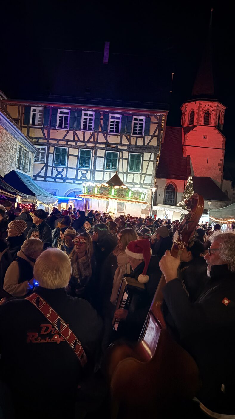 Abendstimmung auf dem Illinger Weihnachtsmarkt – beleuchtetes Fachwerkhaus und rot angestrahlte Stadtkirche mit vielen Besuchern